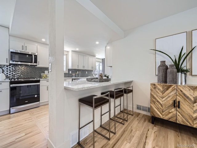 kitchen with white cabinetry, light stone countertops, a kitchen breakfast bar, and appliances with stainless steel finishes