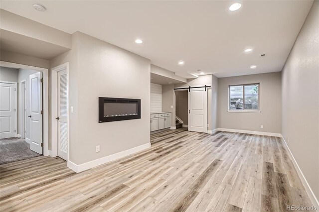 15437 W 95th Ave, Arvada, CO 80007 - unfurnished living room with a barn door, light wood-type flooring, recessed lighting, and a glass covered fireplace