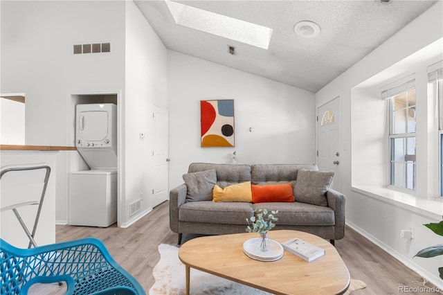 3050 W 107th Pl Unit E, Westminster, CO 80031 - living room with stacked washer and clothes dryer, a skylight, light wood-style flooring, high vaulted ceiling, and a textured ceiling