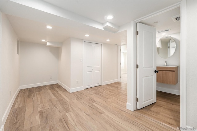 finished basement featuring baseboards, light wood finished floors, and a sink