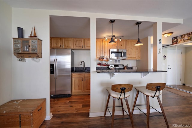 kitchen with pendant lighting, dark wood-type flooring, appliances with stainless steel finishes, and a breakfast bar area