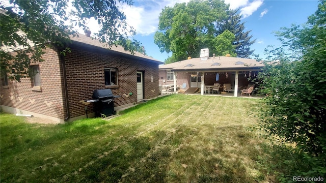 rear view of house featuring a patio area, brick siding, a yard, and a chimney