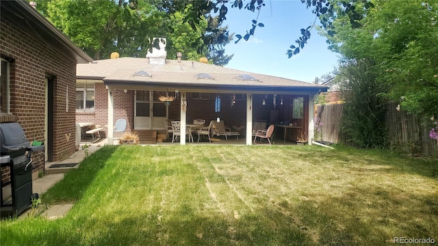 rear view of house featuring entry steps, brick siding, a lawn, and fence