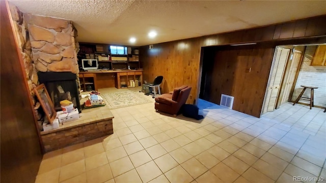 living room featuring light tile patterned floors, visible vents, a textured ceiling, a stone fireplace, and wood walls