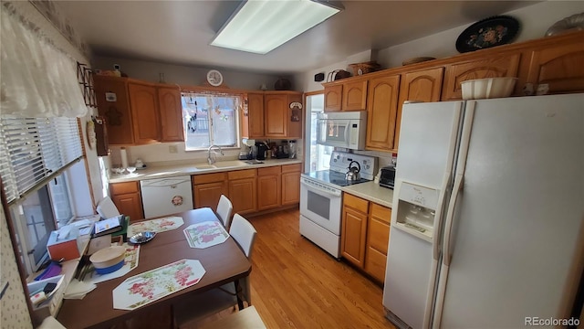 kitchen featuring brown cabinets, light countertops, a sink, light wood-type flooring, and white appliances