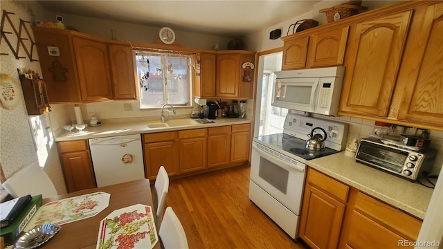 kitchen with light countertops, white appliances, light wood-type flooring, and a sink