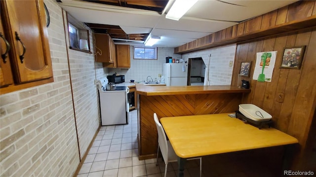 kitchen with brown cabinets, electric stove, a sink, freestanding refrigerator, and light tile patterned flooring