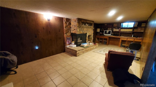 living room with light tile patterned floors, wooden walls, and a stone fireplace