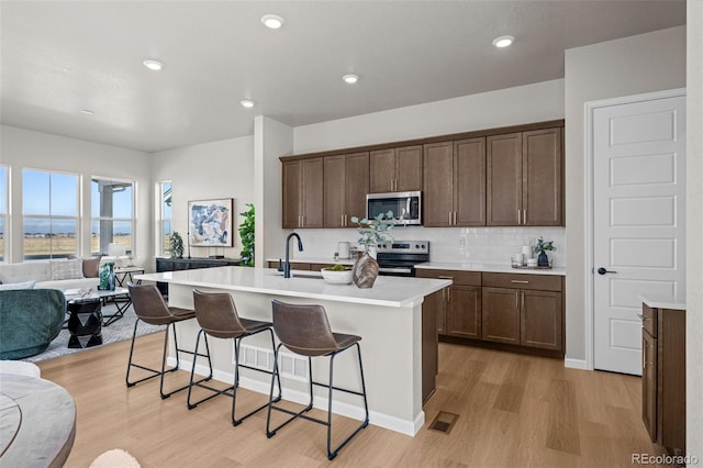 21044 E 63rd Dr, Aurora, CO 80019 - kitchen featuring appliances with stainless steel finishes, open floor plan, light wood finished floors, a kitchen bar, and a kitchen island with sink