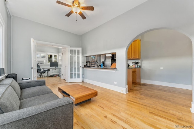 living room featuring baseboards, arched walkways, light wood-style floors, and ceiling fan