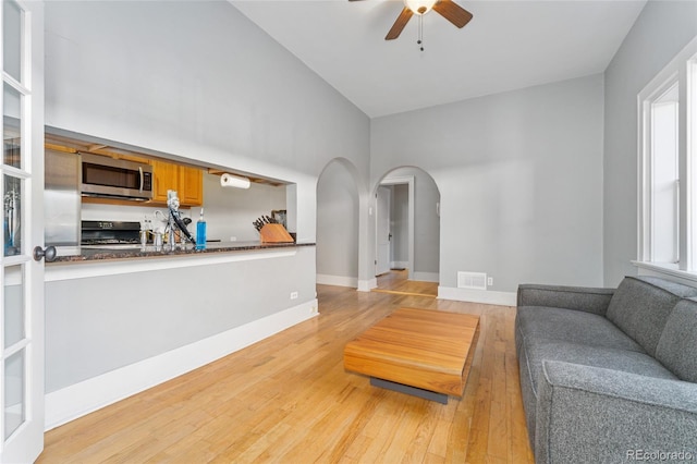 living room featuring a ceiling fan, visible vents, baseboards, light wood-style flooring, and arched walkways