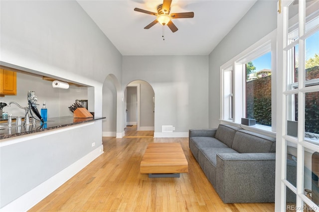 living room featuring light wood-type flooring, arched walkways, baseboards, and ceiling fan