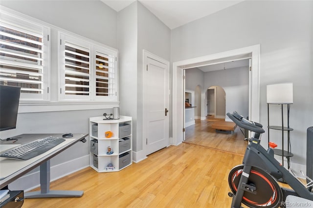 workout area with baseboards, arched walkways, and light wood-style floors