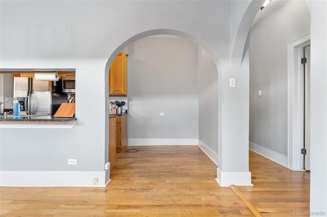 corridor featuring baseboards, arched walkways, and light wood-style flooring