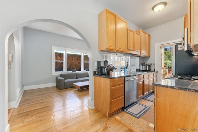 kitchen featuring light wood finished floors, baseboards, dark stone counters, stainless steel appliances, and a sink