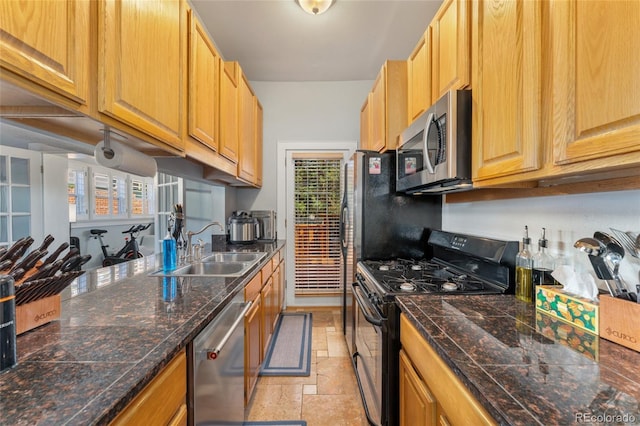 kitchen with a sink, stainless steel appliances, stone tile flooring, and tile counters