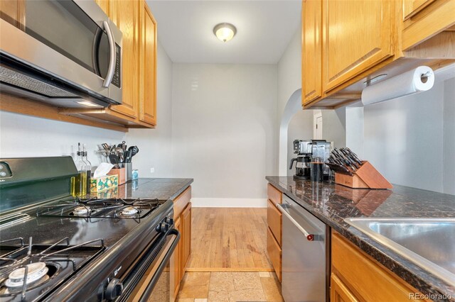 kitchen featuring dark countertops, baseboards, appliances with stainless steel finishes, and a sink