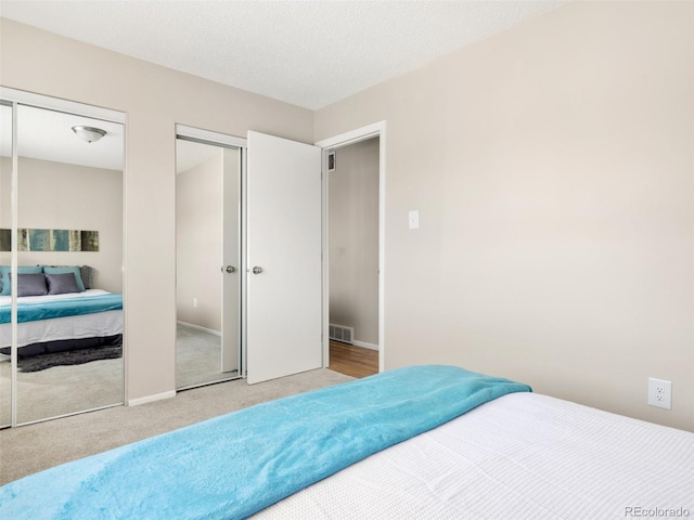 bedroom featuring two closets, light colored carpet, and a textured ceiling