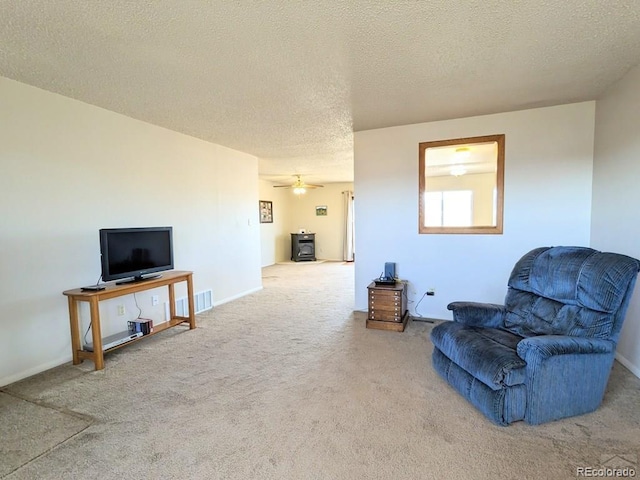 living area with a wood stove, ceiling fan, carpet floors, and a textured ceiling