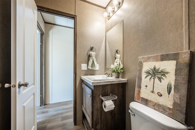 bathroom featuring toilet, vanity, hardwood / wood-style flooring, and ornamental molding