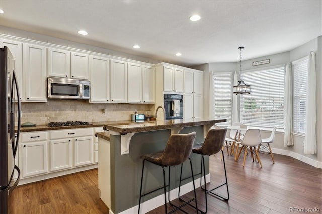 kitchen featuring appliances with stainless steel finishes, pendant lighting, white cabinets, dark wood-type flooring, and a center island with sink