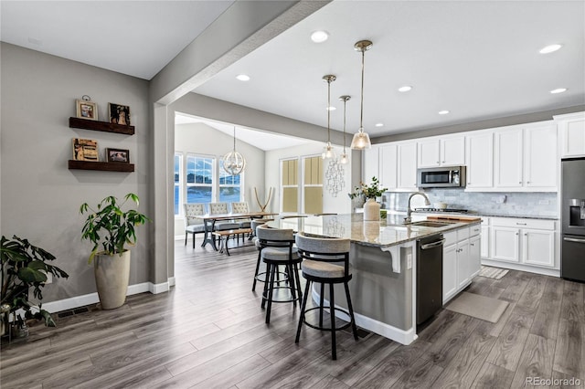 kitchen with light stone countertops, appliances with stainless steel finishes, white cabinetry, and a center island with sink