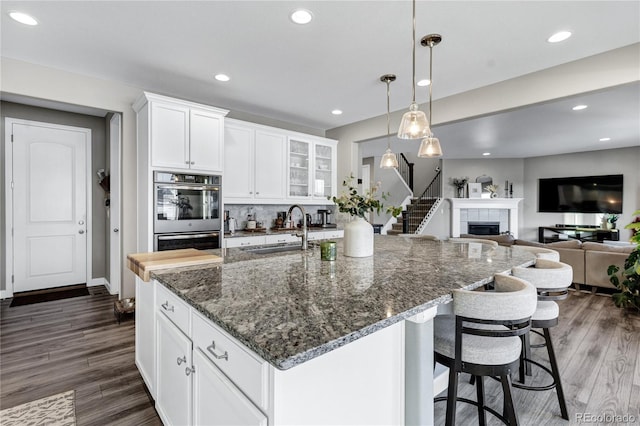 kitchen with sink, white cabinetry, double oven, and an island with sink