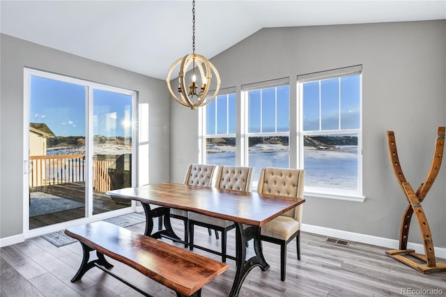 dining room with hardwood / wood-style flooring, a notable chandelier, a water view, and vaulted ceiling