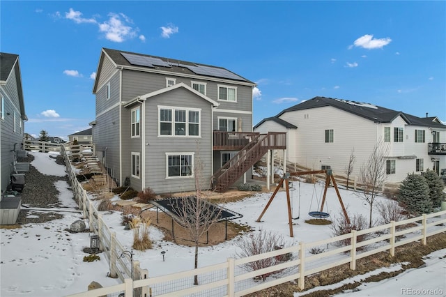 snow covered house with a wooden deck and solar panels