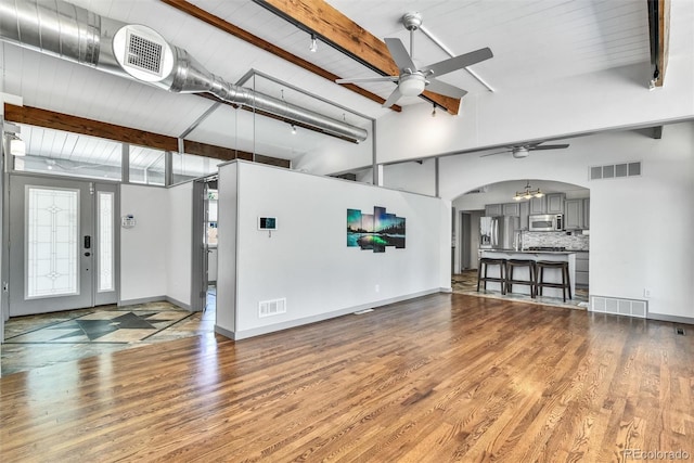 unfurnished living room with beam ceiling, hardwood / wood-style flooring, a towering ceiling, and ceiling fan