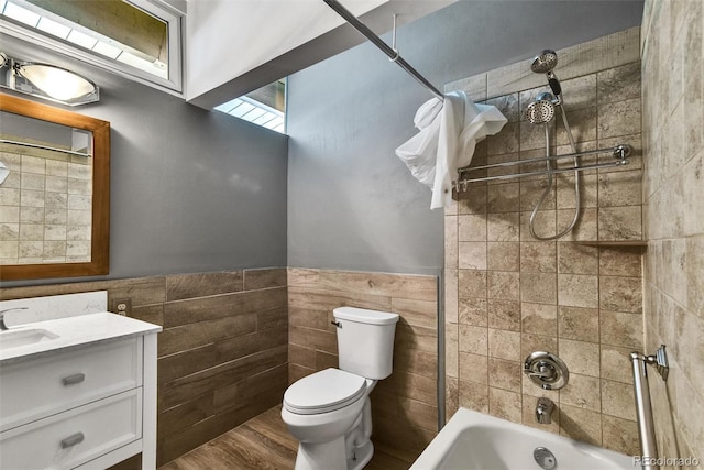 full bathroom featuring tile walls, toilet, vanity, tiled shower / bath combo, and wood-type flooring