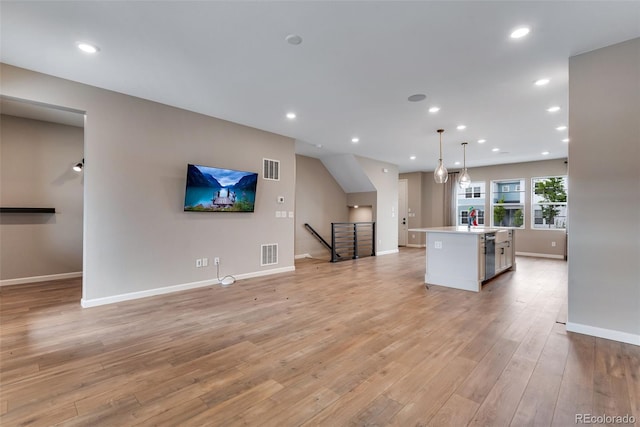 kitchen with sink, white cabinetry, a kitchen island, decorative light fixtures, and light wood-type flooring