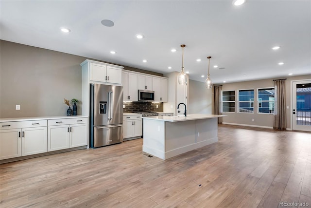 kitchen featuring pendant lighting, appliances with stainless steel finishes, light hardwood / wood-style floors, an island with sink, and white cabinets