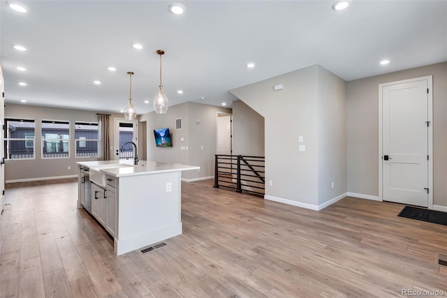 kitchen featuring pendant lighting, white cabinetry, an island with sink, dishwasher, and light wood-type flooring