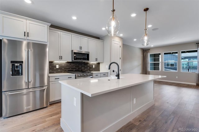 kitchen featuring sink, white cabinetry, decorative light fixtures, premium appliances, and a kitchen island with sink