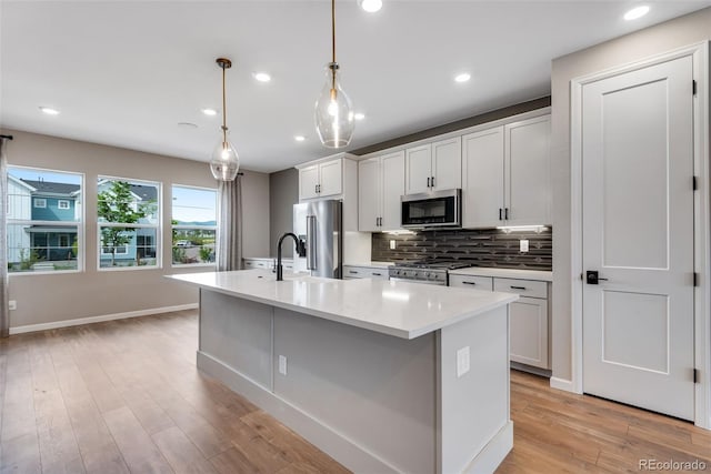 kitchen with white cabinetry, hanging light fixtures, stainless steel appliances, a center island with sink, and light wood-type flooring