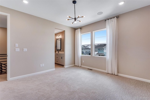 unfurnished bedroom featuring sink, light colored carpet, an inviting chandelier, and ensuite bath