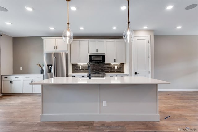 kitchen with appliances with stainless steel finishes, sink, pendant lighting, and a kitchen island with sink