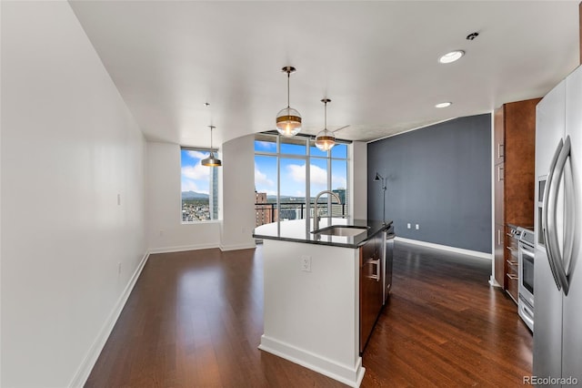 kitchen featuring a kitchen island with sink, sink, hanging light fixtures, appliances with stainless steel finishes, and dark hardwood / wood-style flooring