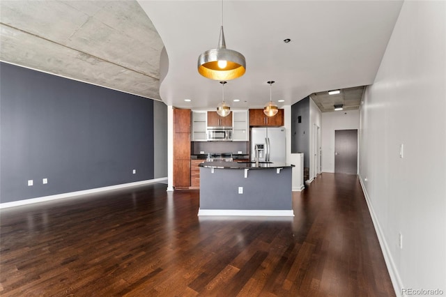 kitchen featuring pendant lighting, stainless steel appliances, an island with sink, and dark wood-type flooring