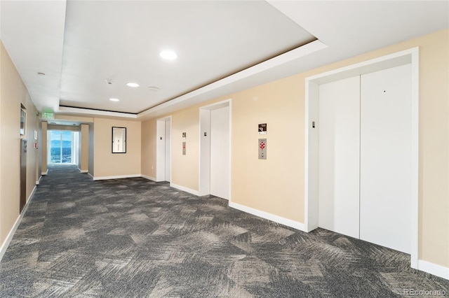 hall featuring elevator, dark colored carpet, and a raised ceiling