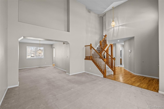 unfurnished living room featuring baseboards, arched walkways, an inviting chandelier, stairs, and carpet floors