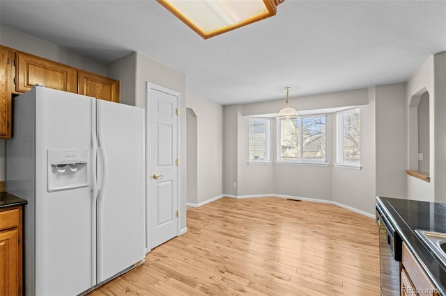 kitchen with white refrigerator with ice dispenser, light wood finished floors, dark countertops, brown cabinetry, and baseboards