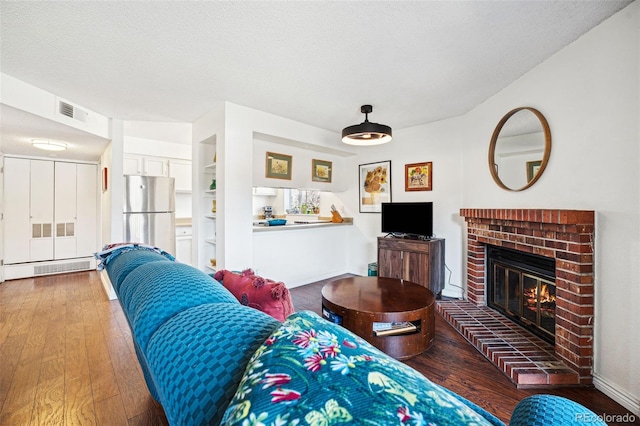 living area with a fireplace, visible vents, a textured ceiling, wood finished floors, and baseboards