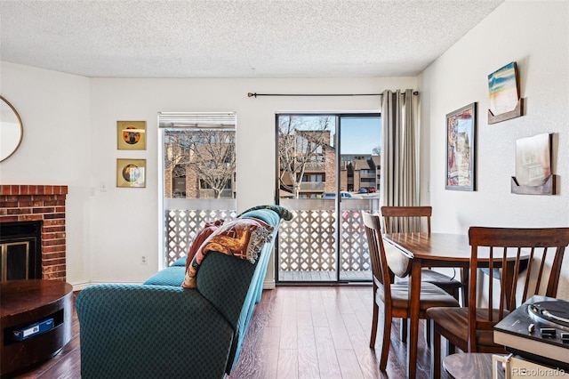 dining room featuring a brick fireplace, a textured ceiling, and hardwood / wood-style flooring