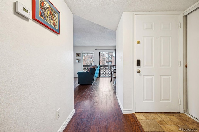 hallway featuring a textured wall, a textured ceiling, baseboards, and wood finished floors