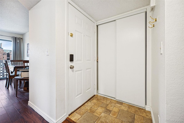 hall featuring stone tile floors, baseboards, a textured ceiling, and a textured wall