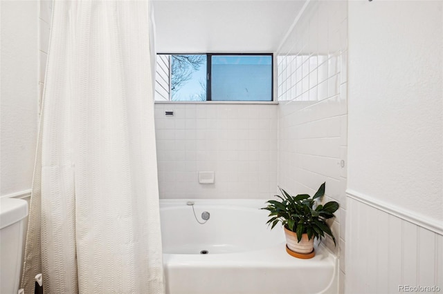 full bath featuring a bathtub, a shower with shower curtain, a wainscoted wall, and toilet