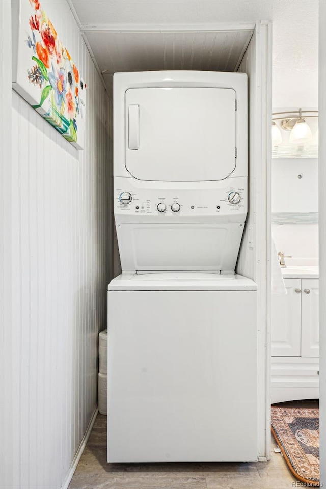 clothes washing area featuring light wood-type flooring, stacked washer and clothes dryer, and laundry area