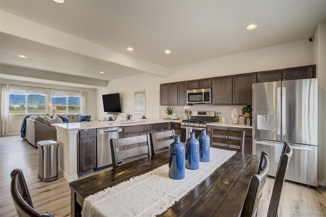 kitchen with open floor plan, stainless steel appliances, dark brown cabinetry, light wood finished floors, and light countertops